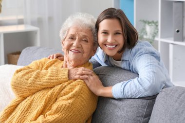 Genç hemşire evdeki kanepede yaşlı kadına sarılıyor.