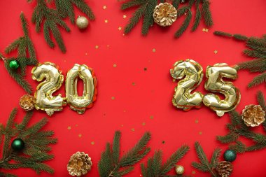 Noel topları, çam kozalakları ve kırmızı arka planda köknar dalları olan folyodan yapılmış 2025 yılı figürü.