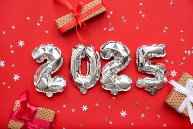 Noel hediye kutuları ve kırmızı arka planda konfetileri olan folyodan yapılmış 2025 model.