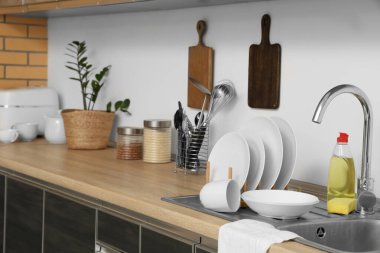 Temiz tabaklar, deterjan ve lavabonun yanında ahşap mutfak tezgahının üstünde sünger.