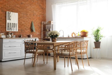 Mutfağın içinde masa, sandalye ve tuğla duvarın yanında güzel kasımpatılar var.