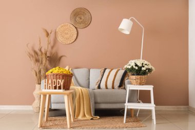 Koltuk, kasımpatı dolu sepetler ve bej duvarın yanındaki oda.