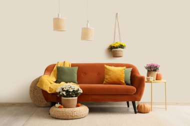 Portakal rengi kanepe ve kasımpatı çiçekleri olan modern oturma odasının içinde.