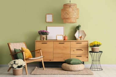 Çekmeceler, koltuk ve kasımpatı çiçekleri yeşil duvarın yanında.