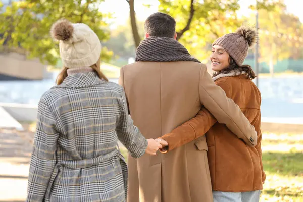 Erkek ve iki güzel kadın, sonbahar parkında yürürken el ele tutuşuyorlar. Poliyamory konsepti
