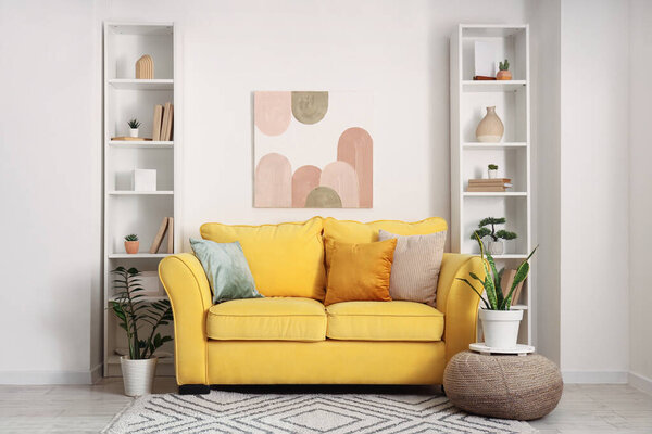 Interior of stylish room with comfortable yellow sofa, houseplants and shelving units