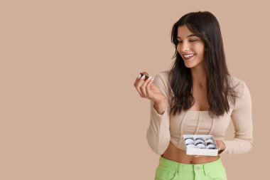 Bej arka planda bir kutu lezzetli çikolata şekeri olan genç bir kadın.