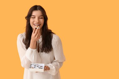 Sarı arka planda çikolata yiyen güzel genç bir kadın.