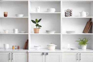 Mutfakta farklı tabaklar ve ev bitkileri olan beyaz raf ünitesi.