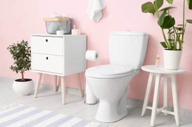 Tuvaletin içinde klozet, komodin ve pembe duvarın yanında bitkiler var.