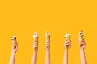 Sarı arka planda waffle külahlı farklı tatlı dondurmalı kadın elleri.
