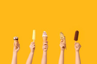 Sarı arka planda farklı tatlı dondurmalı kadın elleri.