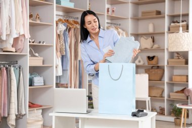 Kadın satıcı elbise mağazasında katlanmış kotları alışveriş çantasına koyuyor.