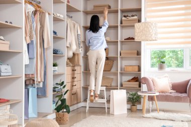 Kadın satıcı giyim mağazasının üst rafından ayakkabı kutusunu alıyor.