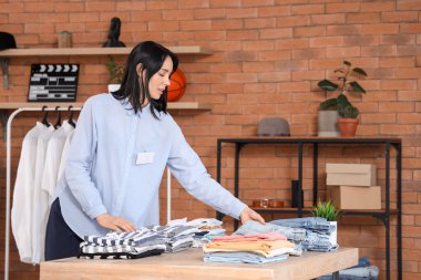 Mağazadaki katlanmış erkek kıyafetleriyle kadın satıcı.