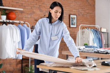 Kadın satıcı, erkek giyim mağazasındaki masada gömlek katlıyor.