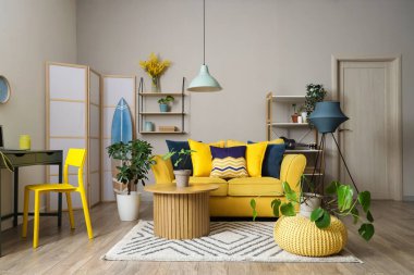 Sarı kanepesi, kahve masası ve çiçekleri olan şık bir oturma odası.