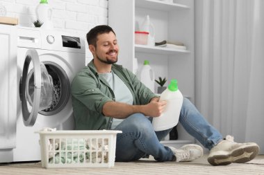 Çamaşır makinesinin yakınındaki çamaşır deterjanı tarifini okuyan genç adam.