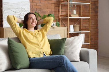 Young woman sitting on grey couch at home