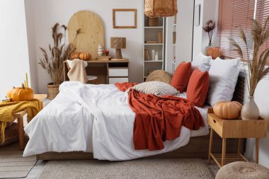 Şık yatak odasının içinde rahat bir iş yeri, vazo dolusu pampa otu, lamba ve balkabağı.