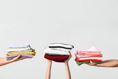 Gri arka planda farklı giysi yığınları olan birçok kadın eli