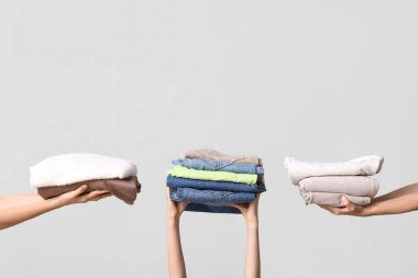 Gri arka planda farklı giysi yığınları olan birçok kadın eli