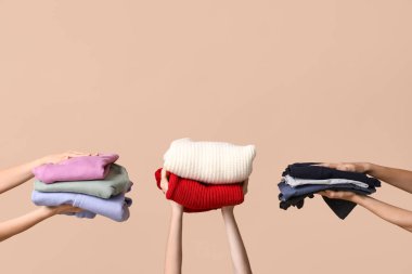 Bej arka planda farklı giysi yığınları olan birçok kadın eli