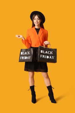 Beautiful young woman with shopping bags on yellow background. Black Friday Sale