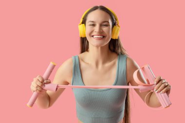 Pembe arka planda genişletici kulaklıklı genç bir kadın.