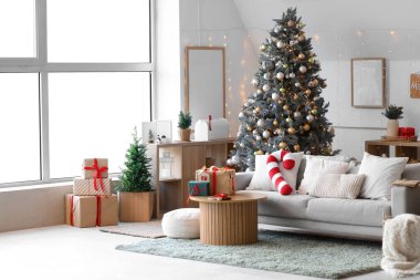 Aydınlık oturma odasının içi gri kanepe, Noel ağacı ve şenlikli dekorasyonlarla dolu.