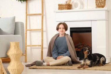 Sıcak battaniyeli küçük çocuk ve evde şöminenin yanında oturan şirin cocker spaniel.