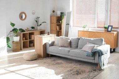 Gri kanepe, raf üniteleri ve bitkilerle aydınlık oturma odasının içinde.