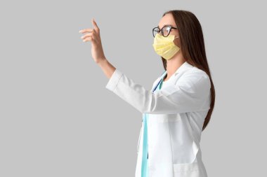 Tıbbi maskeli genç bayan doktor arka planda sanal ekran kullanıyor.