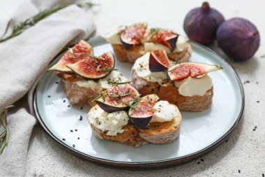 Beyaz zemin üzerinde ricotta peyniri ve biberiyeli lezzetli incirli bruschetta tabağı.