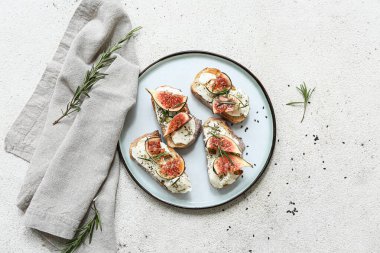 Beyaz zemin üzerinde ricotta peyniri ve biberiyeli lezzetli incirli bruschetta tabağı.