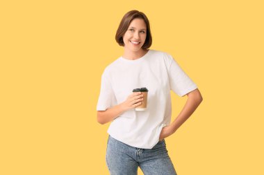 Sarı arka planda kahve fincanı olan boş tişörtlü genç bir kadın.