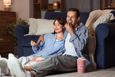 Patlamış mısırlı genç çift akşam evde televizyon izliyor.