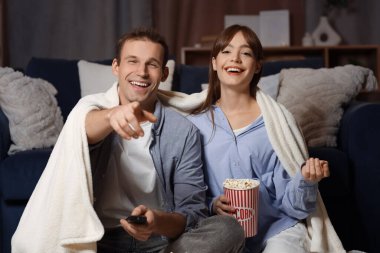 Ekose ve patlamış mısırla gülen genç bir çift akşam evde televizyon seyrediyor.