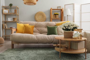 Rahat kanepesi ve kahve masasında kasımpatı çiçekleri olan modern oturma odasının içinde.