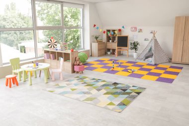 Anaokulunun içinde oyuncaklar, çadır ve masa var.