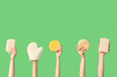 Banyo süngeri ve yeşil arka planda masaj eldiveni olan kadın elleri.