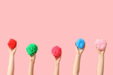 Pembe arka planda farklı banyo süngerleri olan kadın elleri.