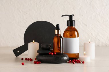 Doğal kozmetik ürünleri şişeleri, spa taşları, yanan mumlar ve beyaz ahşap masa üzerinde şahin dikeni olan kompozisyon