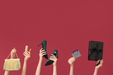 Kozmetik ürünleri olan kadın eller, hediye kutusu, kredi kartı ve kırmızı arka planda aksesuarlar. Kara Cuma İndirimi