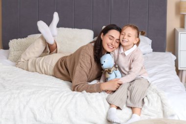 Gülümseyen anne ve küçük kızı yatak odasında oyuncak ayıyla