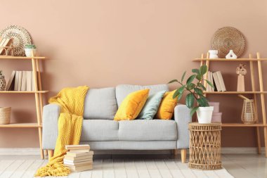 Konforlu kanepe, raf ünitesi, çiçek ve kitap yığını oturma odasının içinde.