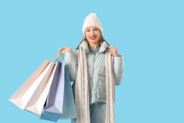 Mavi arka planda alışveriş torbaları olan kışlık giysili güzel bir kadın.