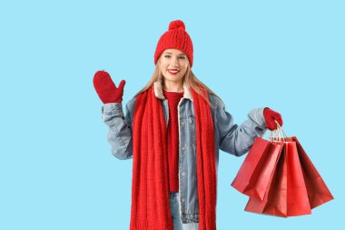 Mavi arka planda alışveriş torbaları olan kışlık giysili güzel bir kadın.