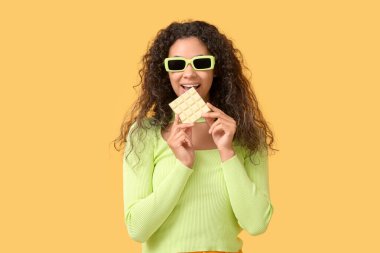 Genç Afro-Amerikalı kadın turuncu arka planda beyaz çikolata yiyor.