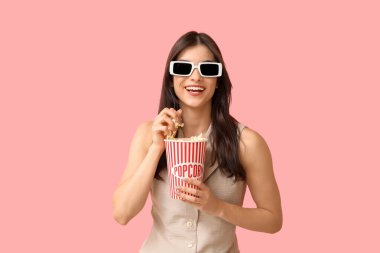 3 boyutlu sinema gözlüklü güzel bir kadın pembe arka planda patlamış mısır yiyor.